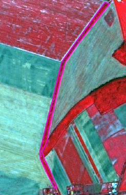 The image is an aerial or satellite false-colour infrared view of an agricultural landscape, likely within Europe. It displays distinct land parcels or fields, primarily in shades of red and green/beige, separated by thin black delineation lines. The red areas typically represent active, healthy vegetation in a false-colour composite, while green/beige areas may indicate different crop types, less vigorous vegetation, or bare soil. A prominent magenta line overlays the image, delineating an irregular boundary across multiple fields. No scale, compass, legend, or specific geographic labels are visible within the image.
