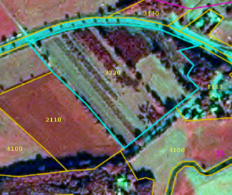 This is a land cover classification map displaying a rural landscape segment with various CORINE Land Cover (CLC) classes, overlaid on satellite or aerial imagery. The map shows several polygons, each assigned a numeric CLC code. A prominent polygon, outlined in light blue, is labelled `3220`, which corresponds to 'Highly Artificial Coniferous Plantations' as defined in the document. This area visually exhibits distinct, linear rows of trees, indicating a cultivated plantation. Other visible land cover classes, outlined in orange, include: - `2110`: Non-irrigated arable land, depicted as a large agricultural field. - `4100`: Areas appearing as agricultural fields or natural vegetation, repeated in multiple locations. - `3110`: Broad-leaved forest, a patch of dense tree cover. - `1111`: Continuous urban fabric, visible near a road in the upper right. The underlying imagery displays a mosaic of cultivated fields, forested patches, and artificial surfaces. No scale bar, compass, or specific date is visible on the map itself.