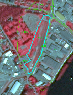 This map displays a false-colour infrared (CIR) satellite image illustrating various land cover types in an urban/industrial environment, typically used for Copernicus Land Monitoring Service (CLMS) land cover classification. The image uses a 1/2/3 band combination, where healthy vegetation appears red, urban structures and bare earth appear in shades of grey and blue, and water bodies are dark blue or black. Key land cover polygons are outlined and labelled with numerical codes, interpreted as CORINE Land Cover (CLC) categories based on the surrounding document context: - A prominent, elongated area in the centre, outlined in light blue, is labelled '1330', representing 'Construction sites, Land without current use, Waste land'. This area shows characteristics of disturbed or disused land. - Areas labelled '1110 (Continuous urban fabric)' are visible towards the top, and '1120 (Discontinuous urban fabric)' are present to the east and north of the central '1330' area, indicating built-up zones. - Linear features and associated land, identified as '1210 (Road and rail networks and associated land)', traverse the image. - An area to the west of the '1330' zone is labelled '1310 (Mineral extraction sites)'. - Adjacent to a body of water at the bottom right, an area is labelled '1220 (Port areas)'. - A large vegetated area, appearing distinctly red in the CIR composite, is located in the upper left portion of the image.